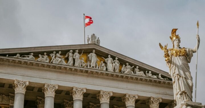 Front view of Austrian Parliament Building with Athena statue and national flag.