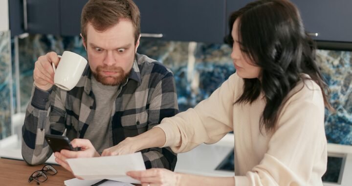 A couple reviews household bills in a kitchen, appearing concerned and focused.